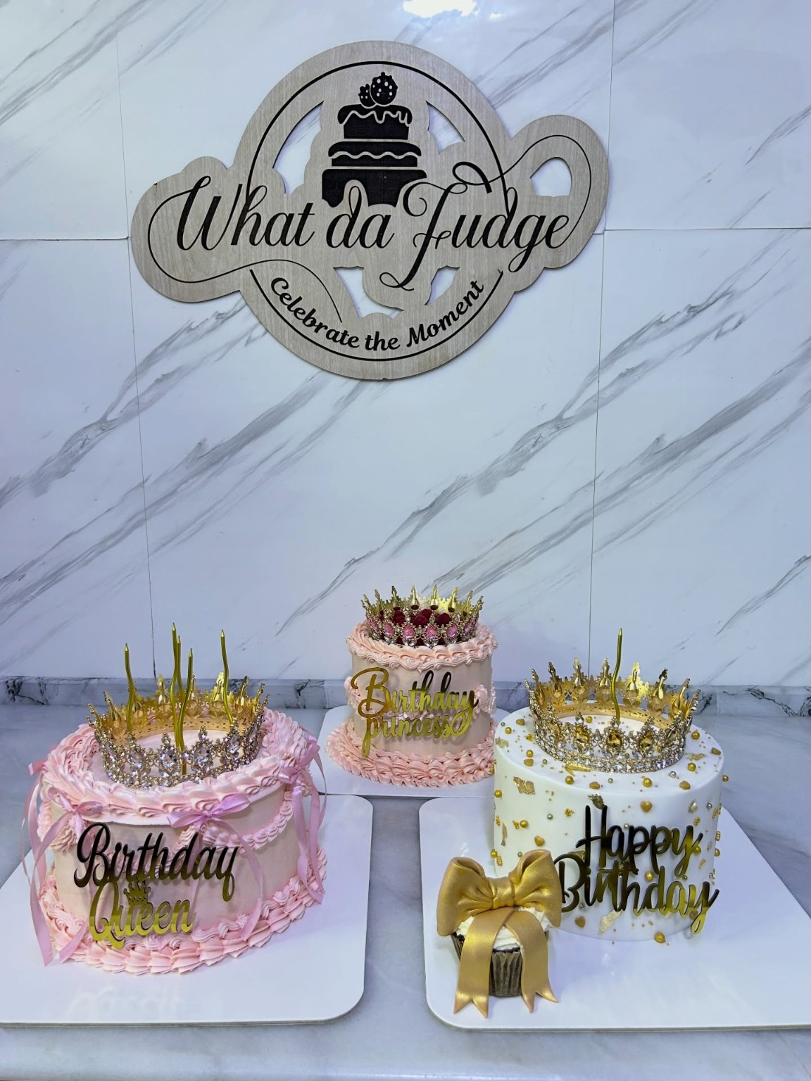 مجموعة تورت عيد ميلاد وردية وبيضاء بتفاصيل ذهبية داخل استوديو What Da Fudge